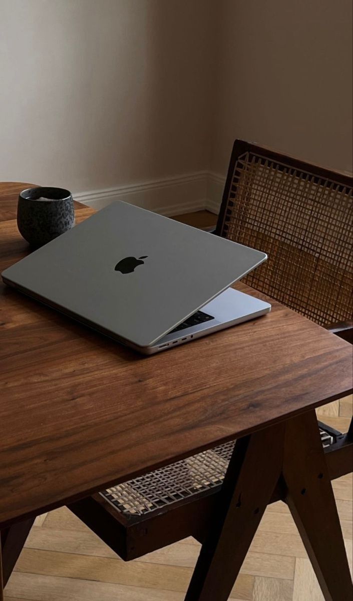 Closed laptop and ceramic mug on a walnut desk with a cane chair